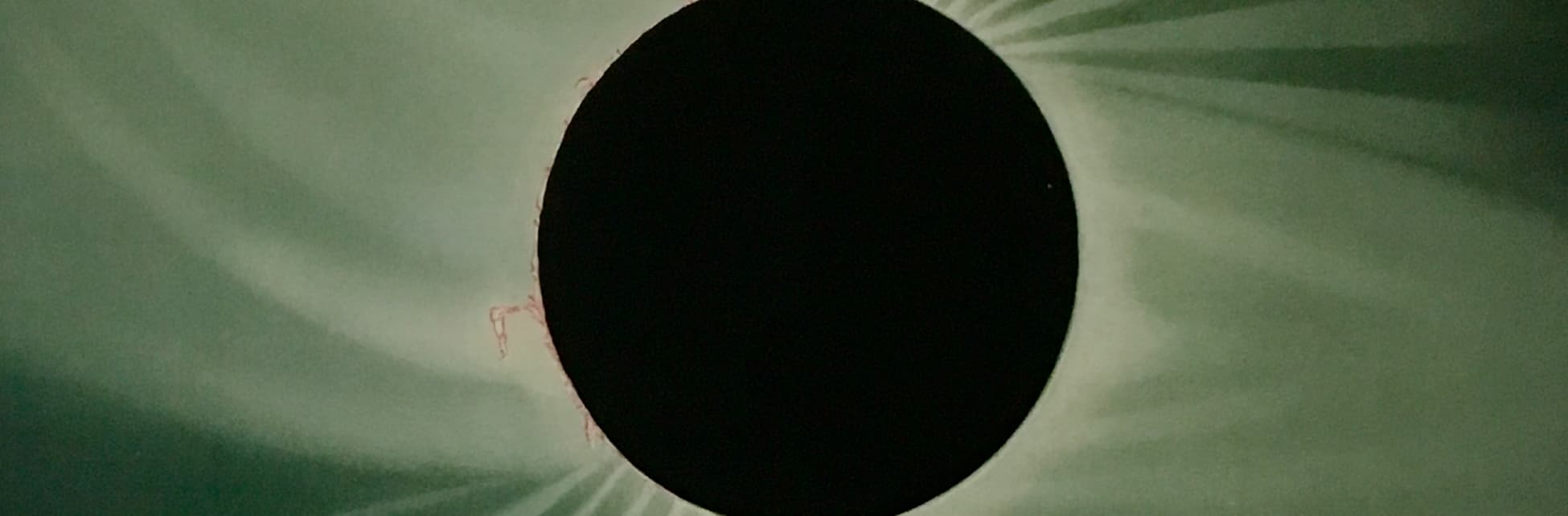 Ilustración. Sobre un fondo en tonos verdes, destaca un círculo negro en el centro de la imagen, rodeado por un anillo de luz.