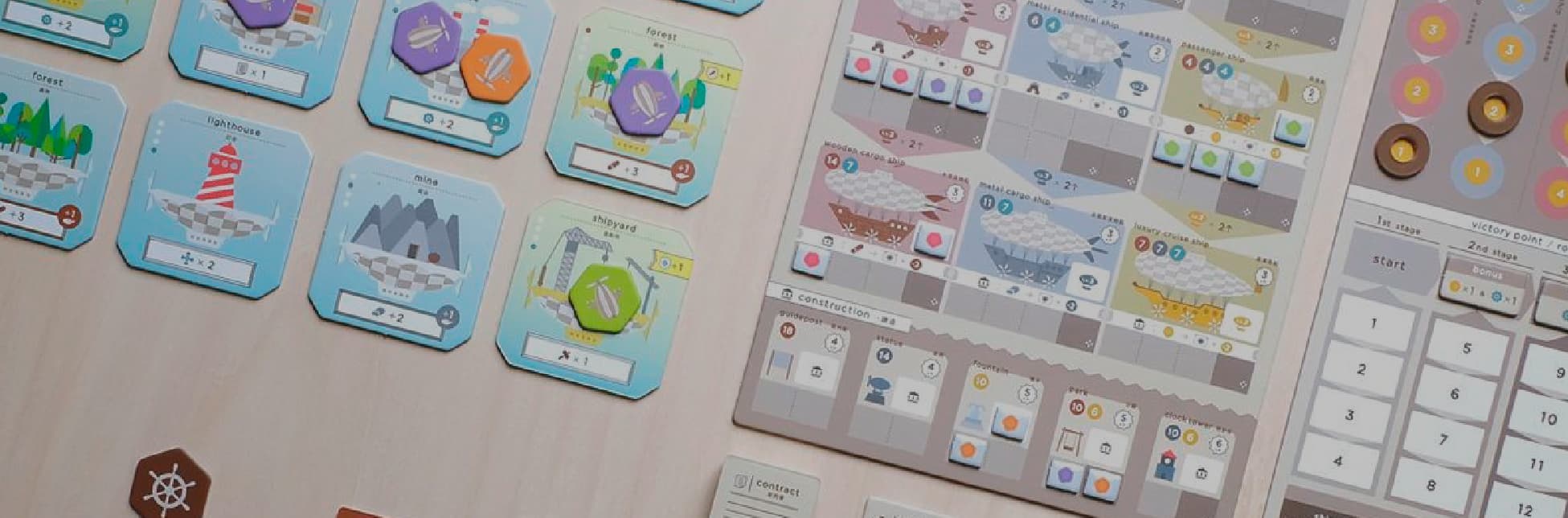 Fotografía. Sobre una superficie de madera clara se distribuyen componentes de un juego de mesa: fichas hexagonales, tarjetas ilustradas con símbolos de fábricas, bosques, contratos y dirigibles, y tableros con íconos, números y casillas de colores.