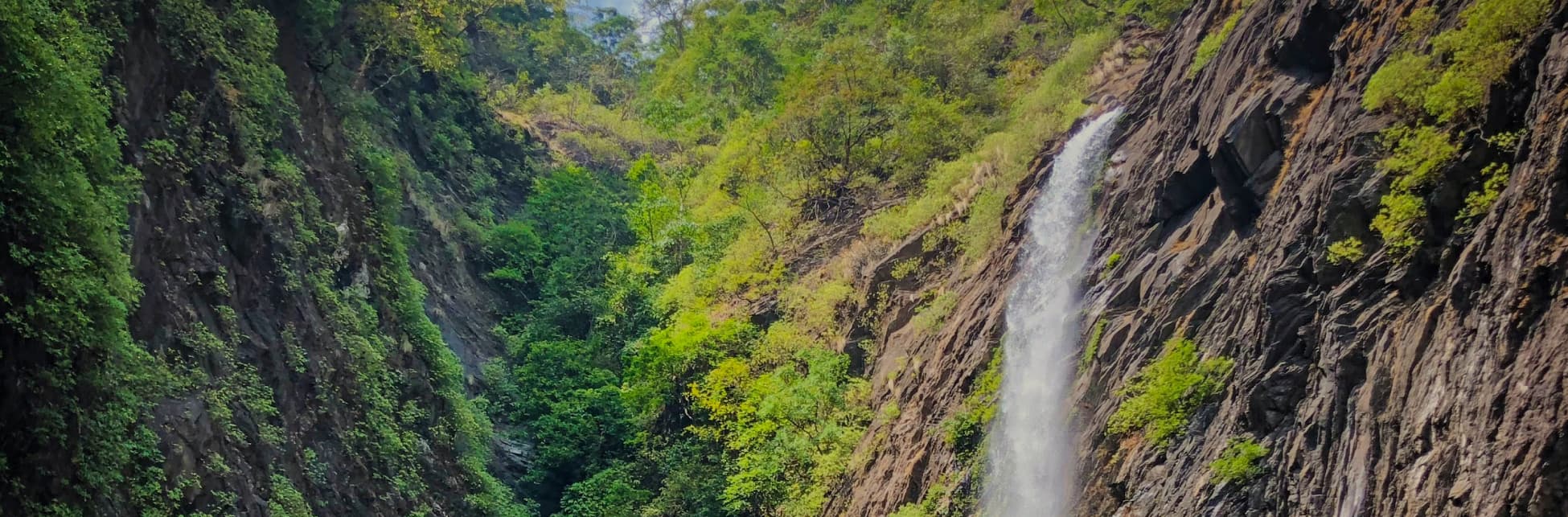 Ilustración. En el fondo, una cascada cae entre montañas cubiertas de vegetación bajo un cielo parcialmente nublado.