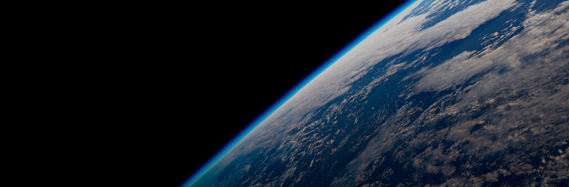Afiche. Sobre un fondo negro se observa una fotografía de la Tierra desde el espacio, mostrando el horizonte curvado del planeta con nubes blancas sobre el océano.