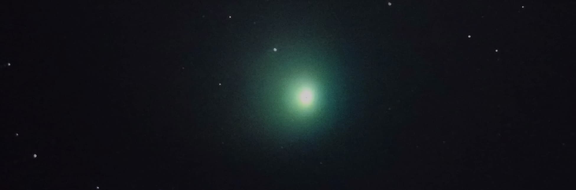 Foto. Sobre un fondo estrellado aparece en la parte superior de la imagen un punto brillante en tonos verdes. 