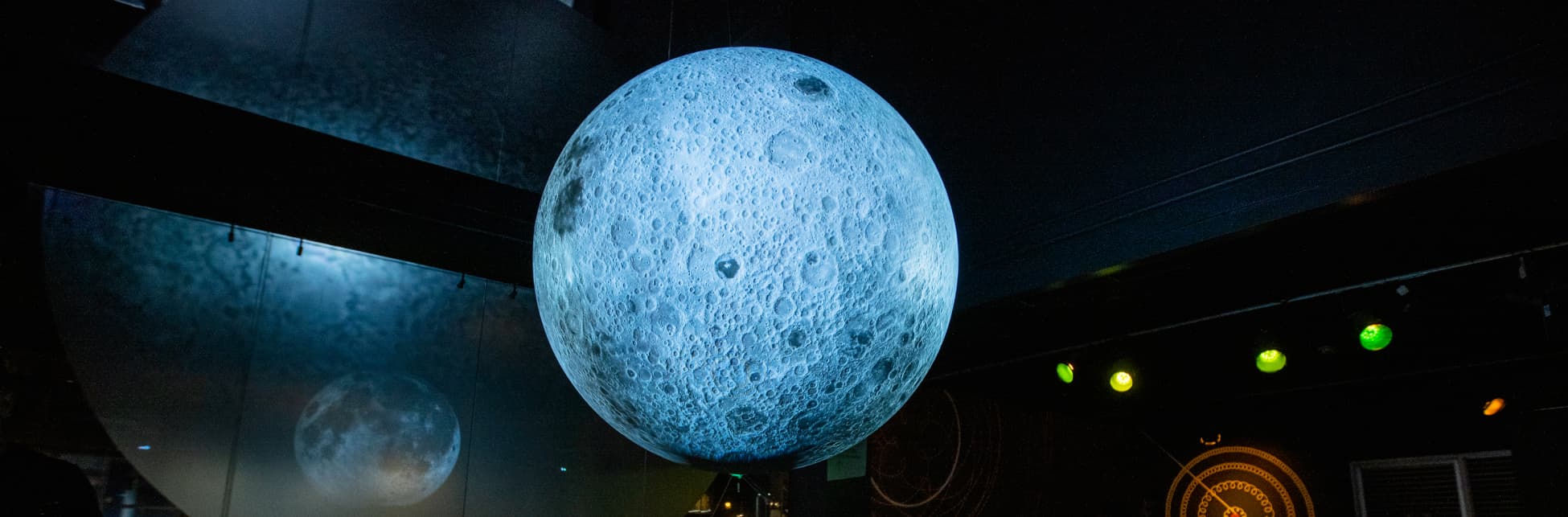 Foto. En la parte derecha de la imagen una esfera con la superficie de la Luna en medio de un salón. 