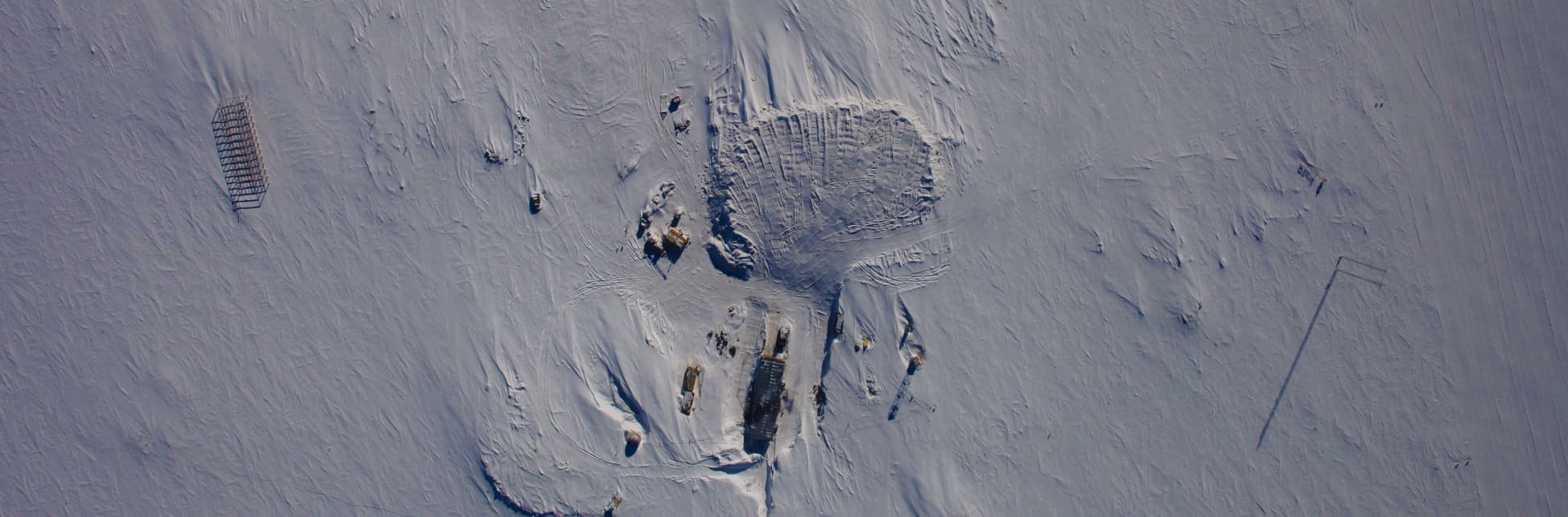 Foto. En la parte inferior derecha de la imagen, tomada desde arriba, se observan algunos edificios dispersos sobre la nieve. 