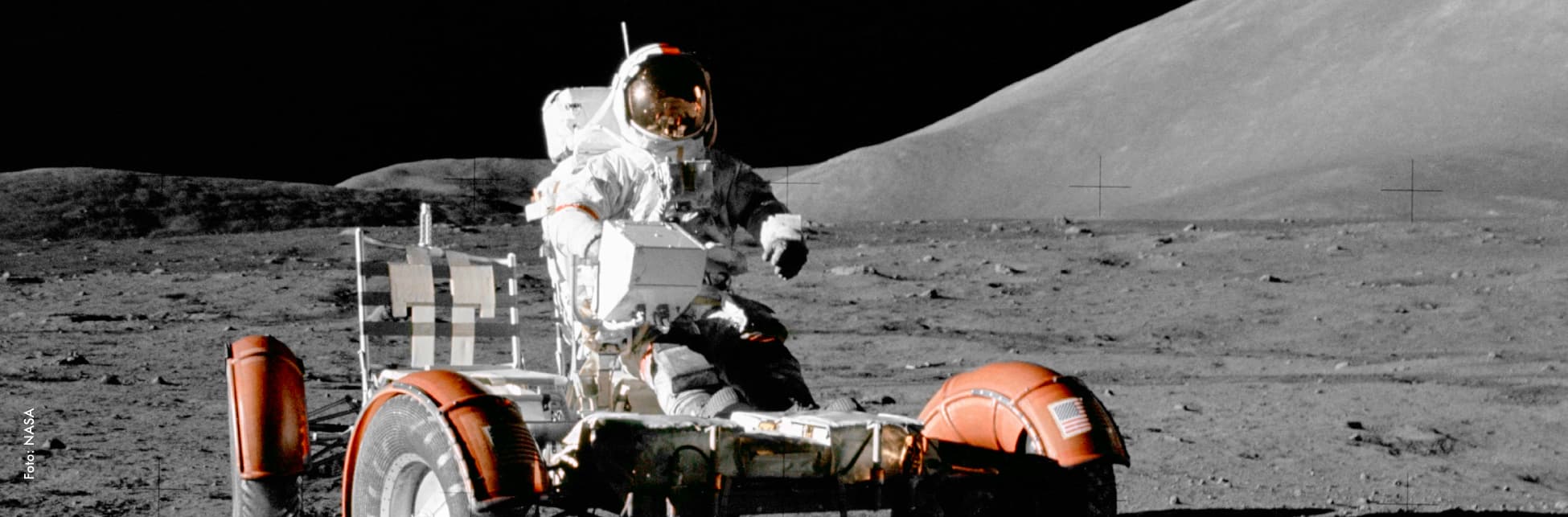 Foto. Sobre un fondo rocoso aparece un artefacto con ruedas y sobre él un astronauta. 