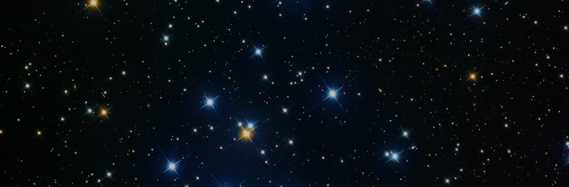Foto. Un fondo estrellado en el que resaltan algunas zonas con estrellas más grandes y brillantes, en tonos azules y naranjas.