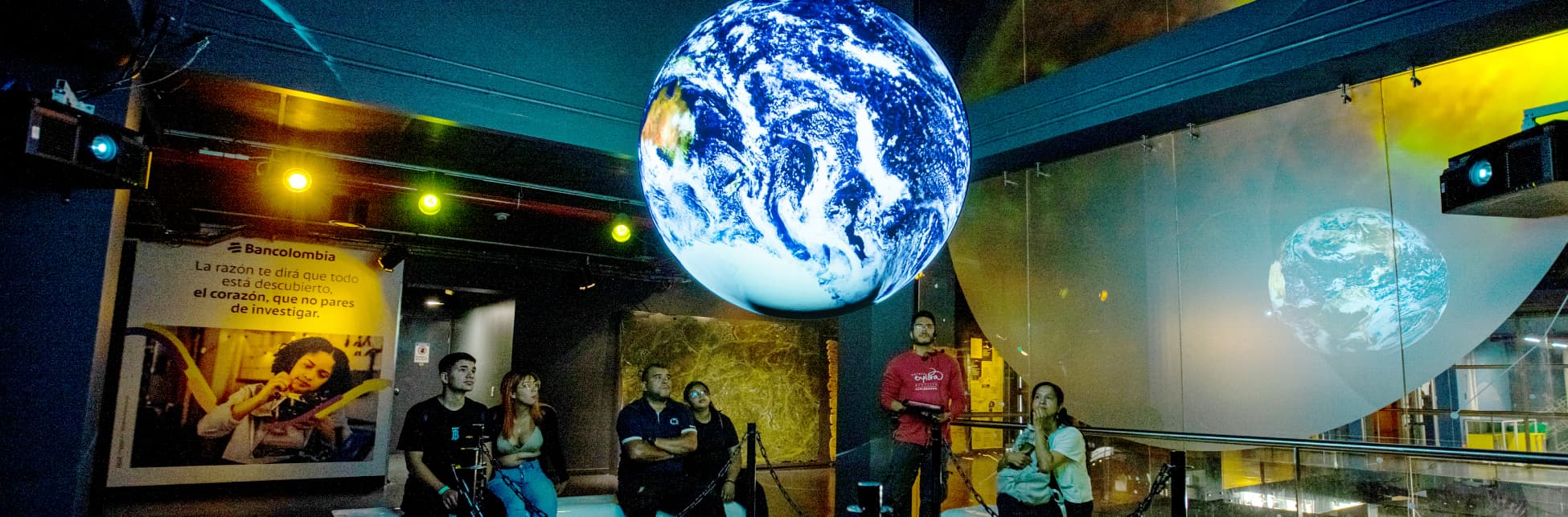Foto. En un espacio amplio hay en el centro un globo terráqueo flotando, varias personas miran con atención la esfera. 