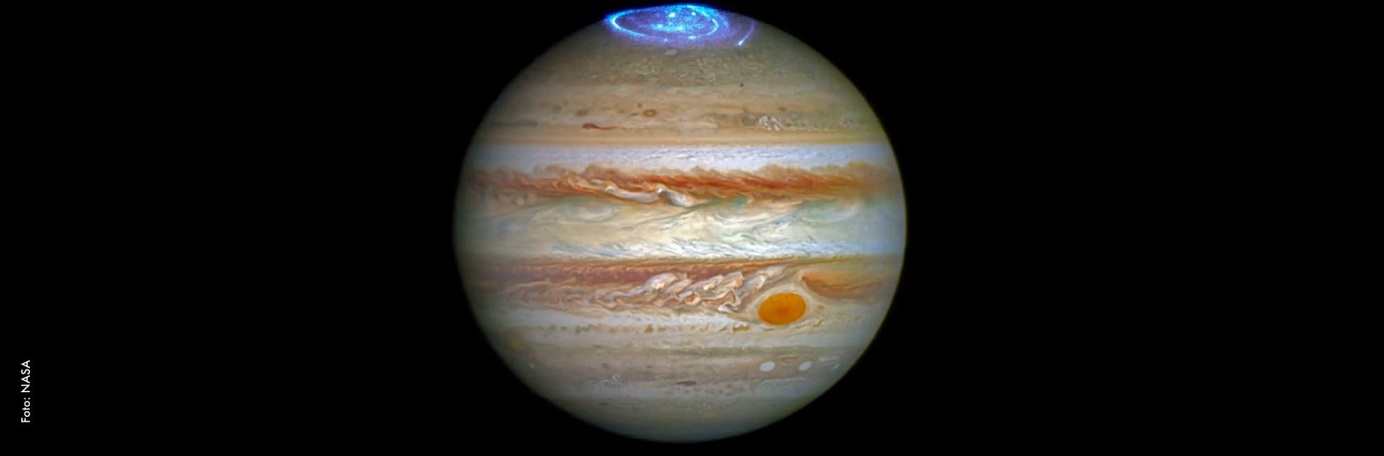 Foto. En el centro de la imagen el planeta Júpiter un círculo con franjas que se intercalan en tonos naranjas y blancos. En la parte superior de él una espiral color azul fosforescente.