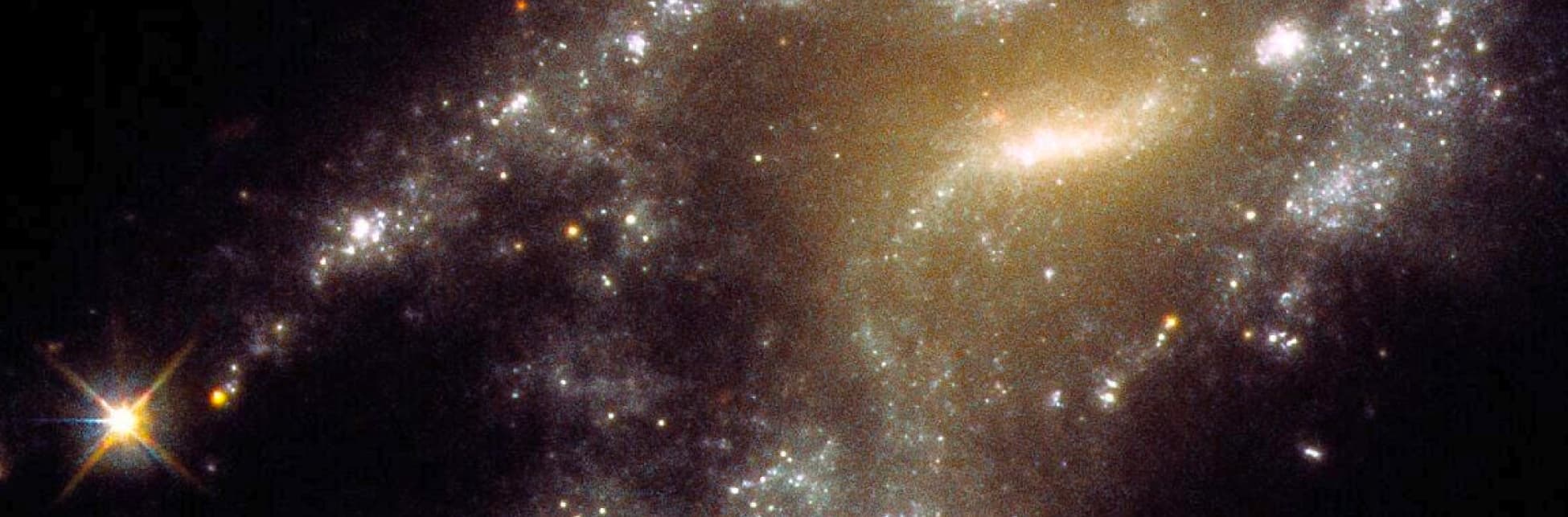Imagen. Sobre un fondo espacial lleno de estrellas y galaxias, se destaca una estructura brillante con múltiples cúmulos estelares dispersos, formando un patrón similar a collares de perlas en el universo profundo.