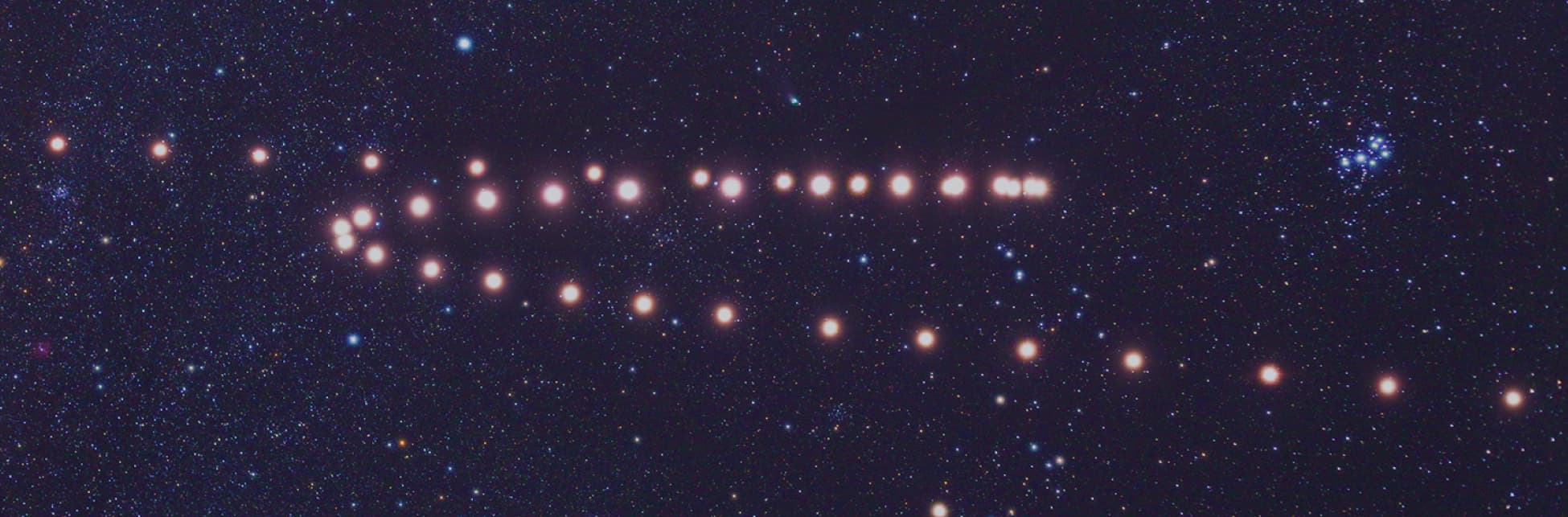 Foto. Sobre un fondo estrellado aparece en el centro de la imagen una secuencia de puntos brillantes rojizos que forman lo que parece una letra z.