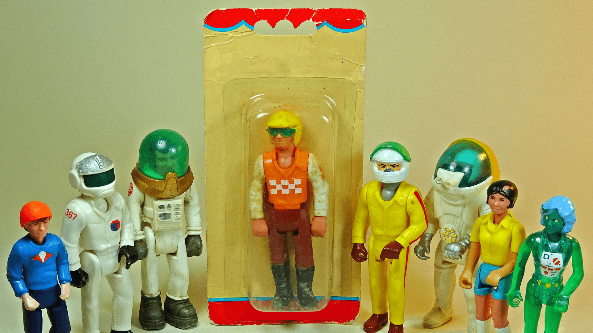 Fotografía. Aparecen de pie 8 muñecos de juguete. Unos tienen figuras humanas, otras de astronauta y otras de robot. El del medio está guardado en su empaque.