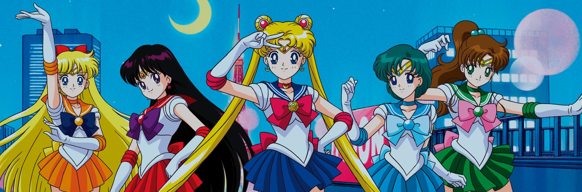 Ilustración. Sobre un fondo que representa un cielo nocturno con estrellas y una luna creciente, se observa un paisaje urbano estilizado y, en primer plano, cinco personajes femeninos de estilo animé con trajes marineros, dispuestas en formación y realizando poses coreografiadas.