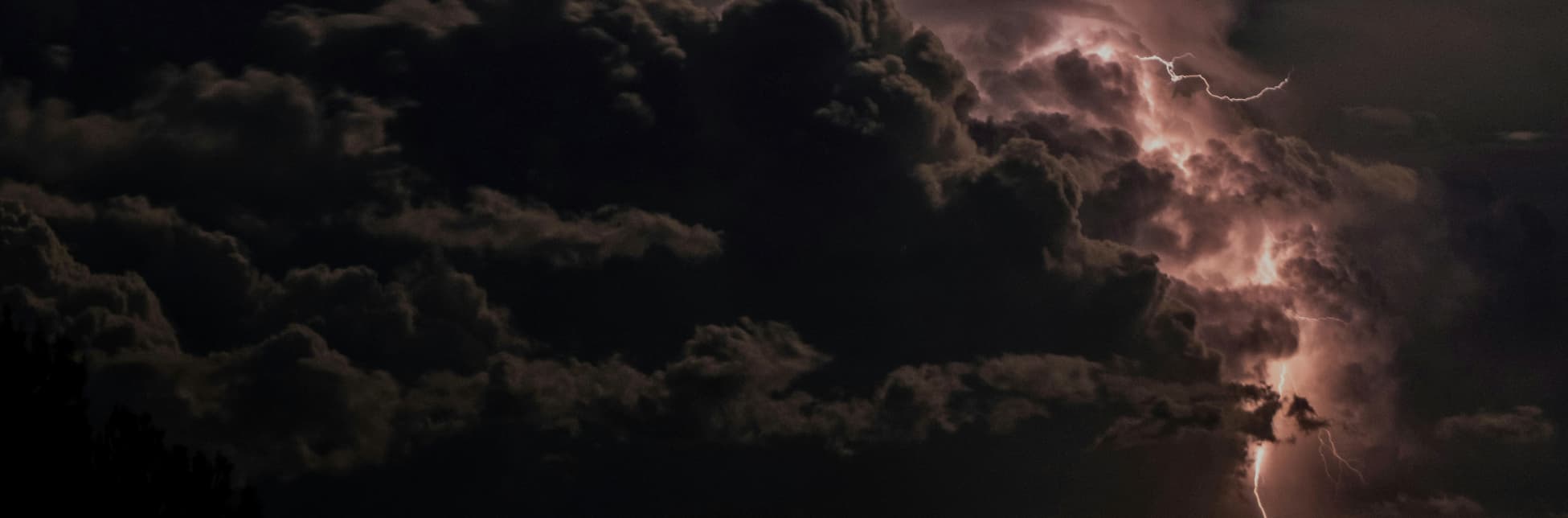 Fotografía. En el fondo se observa una escena nocturna de nubes densas iluminadas desde dentro por relámpagos.