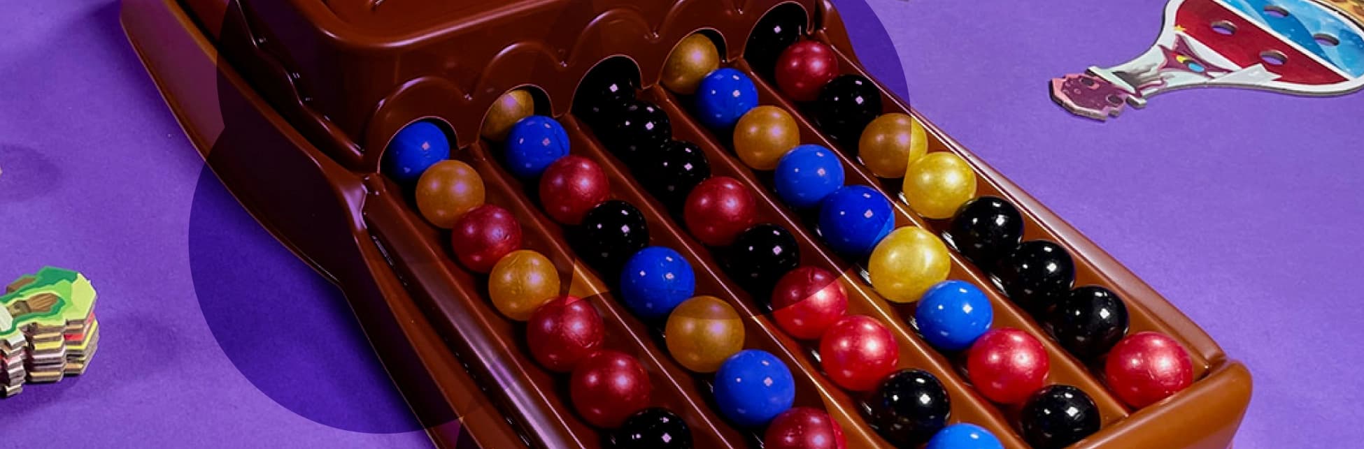 Fotografía de un tablero con esferas de colores organizadas en filas sobre fondo con tonos morados y naranjas.
