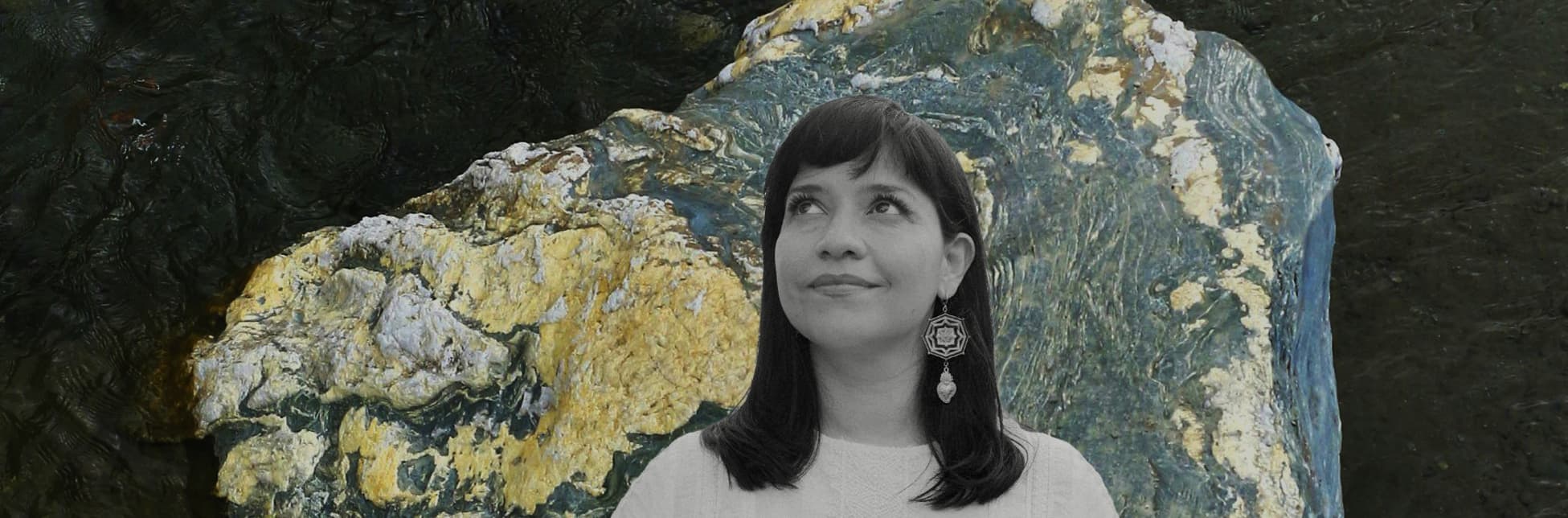 Fotografía. Sobre un fondo con una textura abstracta que recuerda a formaciones minerales y superficies rocosas, se observa en la parte inferior derecha el retrato en blanco y negro de una mujer de frente, con el rostro ligeramente elevado y la mirada hacia arriba, cabello oscuro a la altura de los hombros y blusa clara.