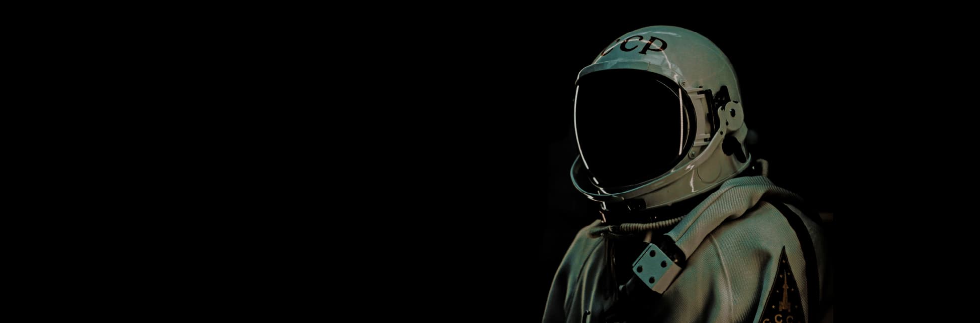Afiche. Sobre un fondo oscuro se observa un astronauta con casco reflectante y traje claro, con detalles y parches visibles en el pecho.