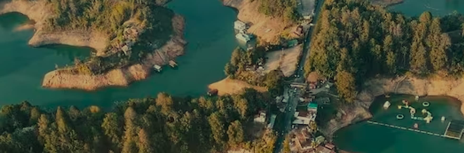 Fotografía aérea de un embalse con islas y un puente vehicular que cruza el agua. A los lados del puente hay construcciones y embarcaciones.