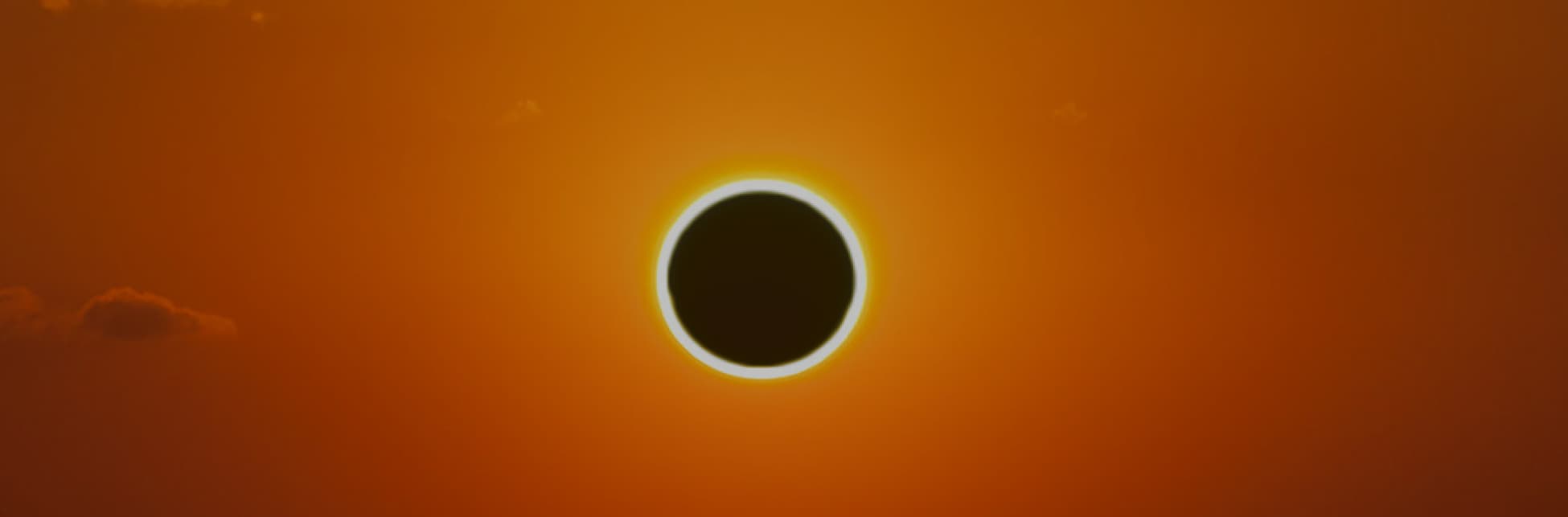 Foto. Sobre un cielo color naranja aparece un círculo negro con borde brillante.