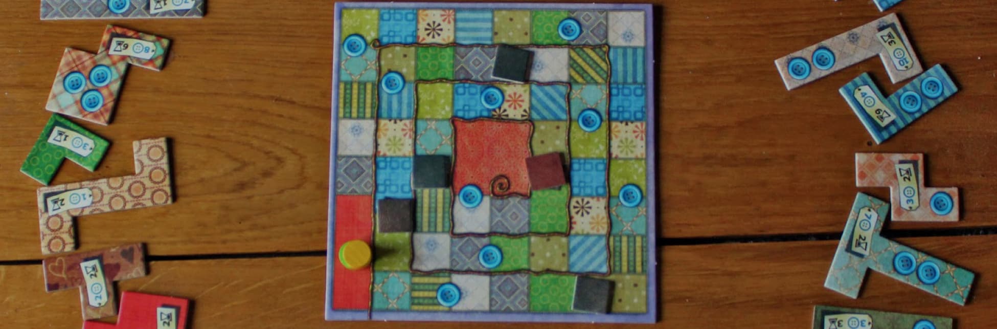 Fotografía. Un tablero de juego de mesa con piezas de diferentes colores y patrones está sobre una superficie de madera, rodeado de fichas dispersas con números y formas variadas.
