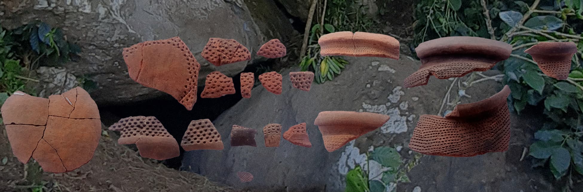 Fotografía. Sobre el suelo y un fondo rocoso cubierto parcialmente por vegetación, se distribuyen fragmentos de cerámica arqueológica de color rojizo, algunos con perforaciones.