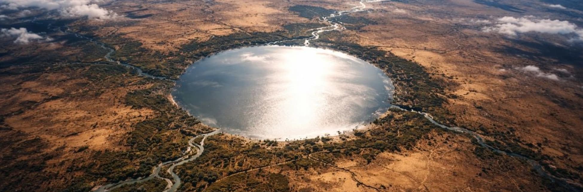 Ilustración. Paisaje árido de color amarillo con un gran lago circular en el centro y caminos sinuosos alrededor.