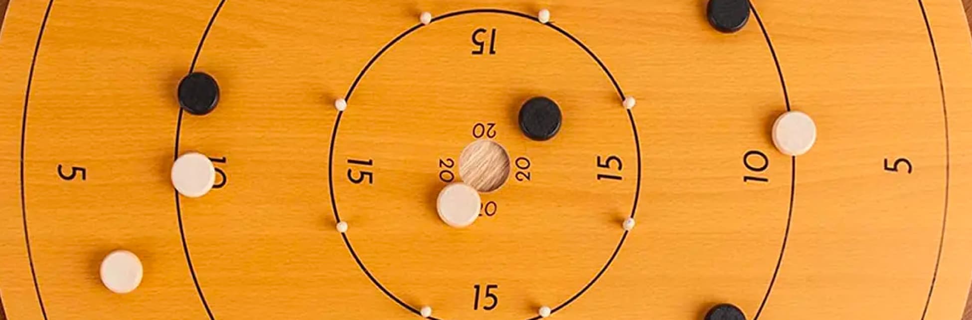Fotografía. Un tablero de juego que cuenta con diferentes círculos que escalan el tamaño, cada circulo contiene un número y en el cetro del tablero hay un agujero. Sobre el tablero diferentes piezas pequeñas.