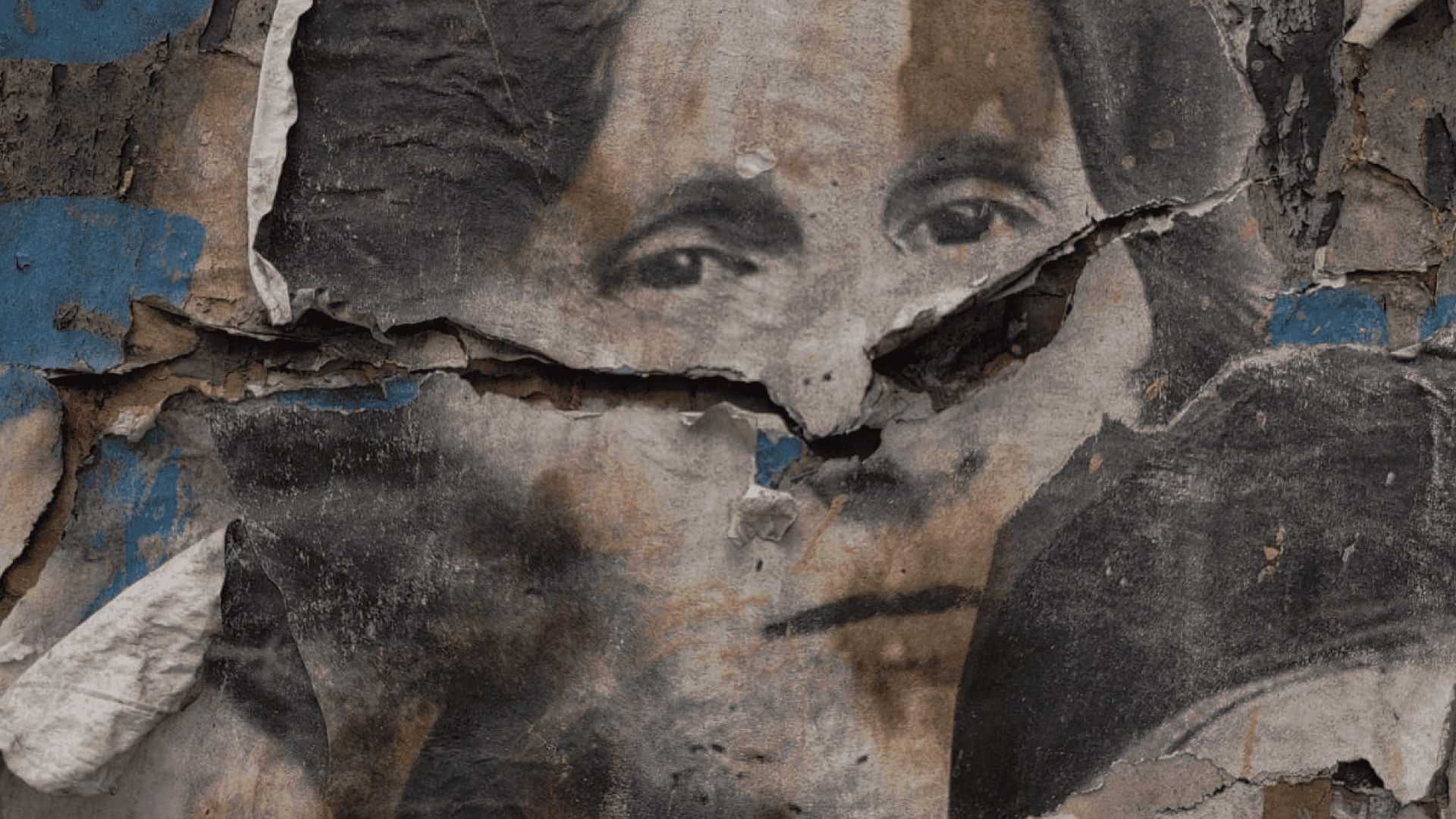 Fotografía. La foto del rostro de una mujer impresa en papel y pegada en un muro. La mujer mira con nostalgia y sobre su nariz el papel está rasgado.