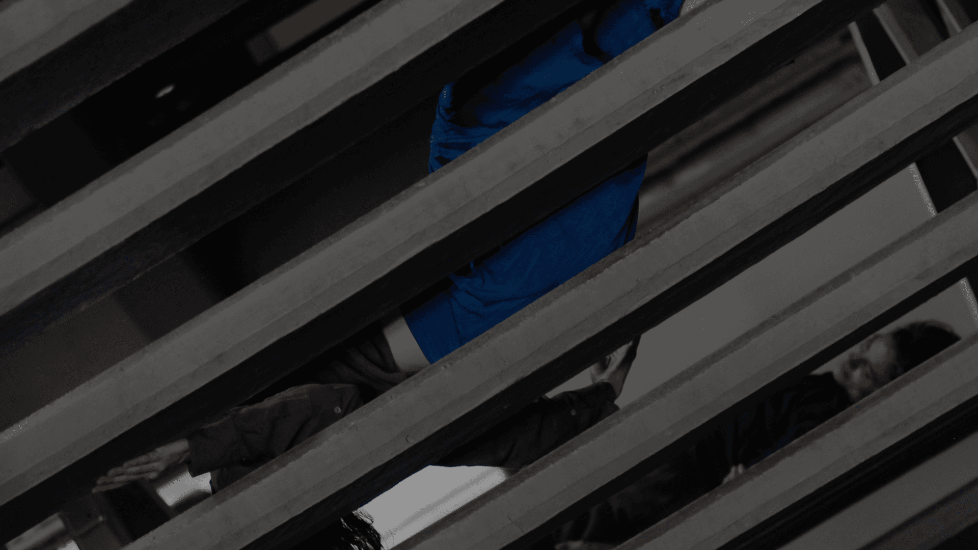 Fotografía. A través de los espacio vacíos de una escalera de cemento aparece la figura de un cuerpo de mujer que está acostado en las escalas.