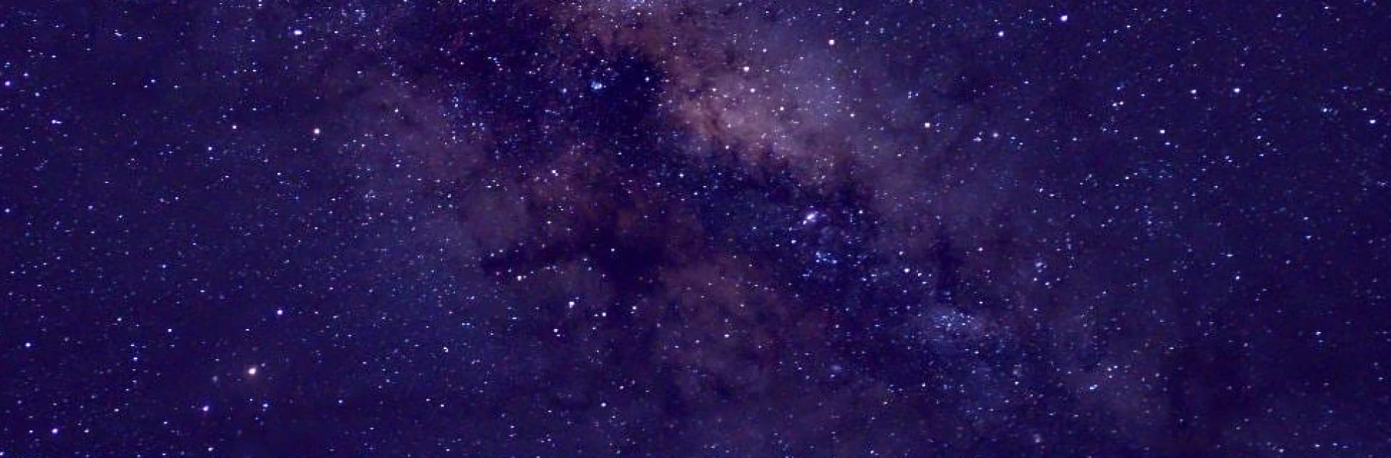 Fotografía. Un cielo nocturno ocupa toda la composición, cubierto por numerosos puntos luminosos de distintas intensidades. En la zona superior y central se extiende una franja irregular y difusa de la Vía Láctea, con concentraciones de estrellas y nubes oscuras de polvo interestelar que atraviesan el campo de visión.