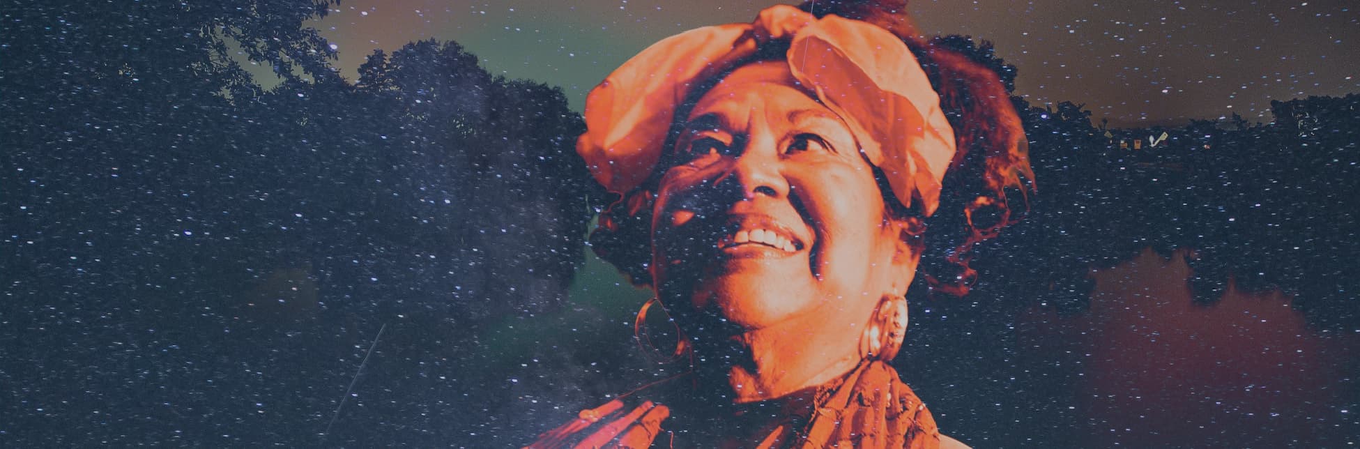 Fotografía de una mujer con turbante y vestimenta tradicional mirando hacia arriba sobre un cielo nocturno estrellado.