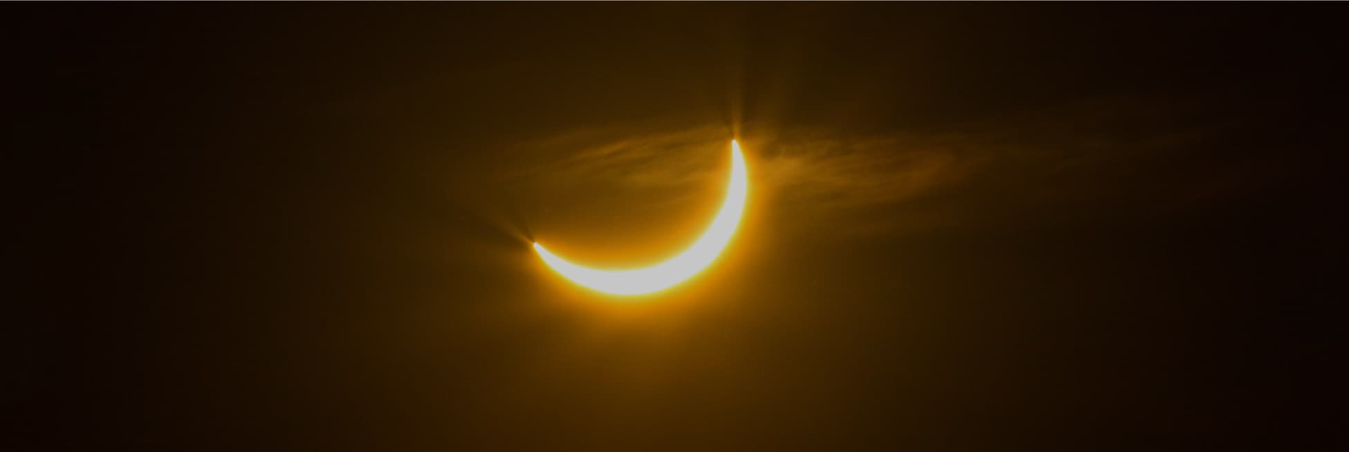 Foto. En el centro de un cielo oscuro con algunas nubes aparece un cachito de algo muy brillante.