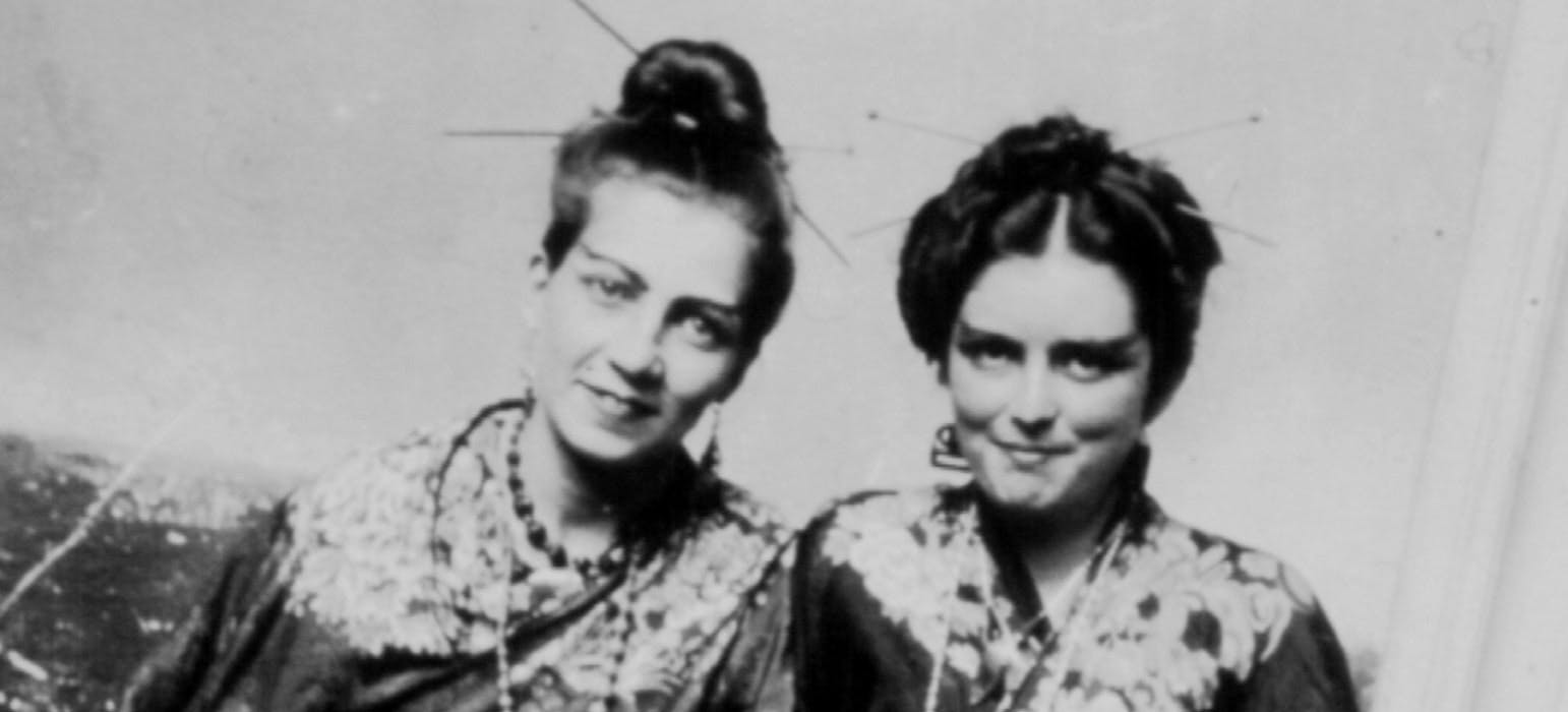 Foto horizontal. En el centro de la imagen dos mujeres sentadas de frente, de medio lado una al lado de la otra. Están disfrazadas con ropa oriental, como geishas.  - Imagen Edith Jiménez y Blanca Ochoa 